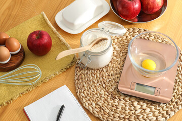 Electronic kitchen scale, products and stationery on wooden table indoors, above view