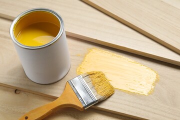 Can of yellow paint and brush on wooden planks