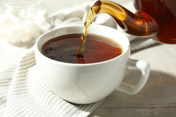 Pouring aromatic tea from teapot into cup at light textured table, closeup