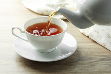 Pouring aromatic tea into cup from teapot at wooden table, closeup