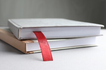 Book with red ribbon bookmark and colorful one on light table against grey background, closeup