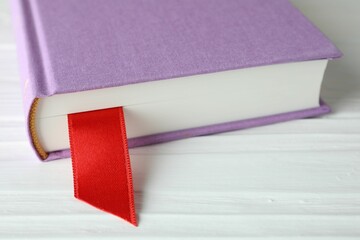 Book with red ribbon bookmark on white wooden table, closeup