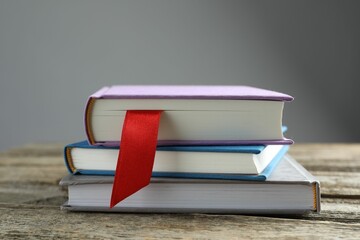 Book with red ribbon bookmark and colorful ones on wooden table against grey background, closeup