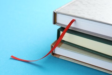 Book with red ribbon bookmark and colorful ones on light blue background, closeup