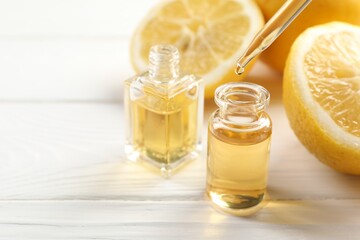 Dripping aromatic essential oil from pipette into perfume bottle and lemons at white wooden table, closeup. Space for text