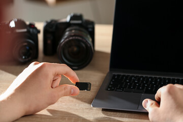 Man inserting SD memory card into laptop at wooden table indoors, closeup