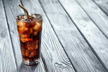 Refreshing cola with ice cubes and straw in glass on grey wooden table, closeup. Space for text