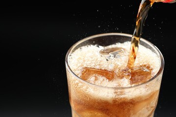Pouring refreshing cola into glass on black background, closeup. Space for text