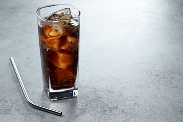 Refreshing cola with ice cubes in glass and straw on grey textured table, closeup. Space for text