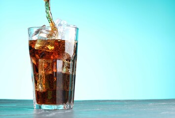 Pouring refreshing cola into glass at dark table against turquoise gradient background. Space for text