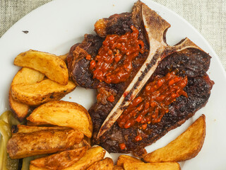 Cooked beef T bone steak with red hot spicy sous. Premium high quality meat served on a plate with...