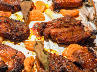 Cooked pork belly portions, tangerine segments and basil fresh herb on cooking foil and metal cooking tray. Marinated meat ready to be cooked in an oven. Tasty meal. Close up.