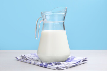 Fresh milk in jug on white wooden table against light blue background