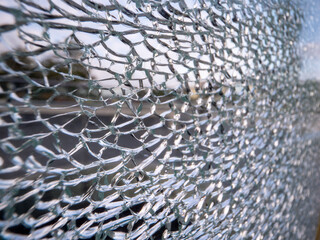 A window with a lot of cracks in it. The glass is shattered and the view is distorted. Result of an accident of intentional anti social behavior in a city. Scene of vandalism.