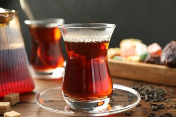 Traditional Turkish tea in glass cups, teapot, dry leaves, brown sugar and sweets on wooden table, closeup