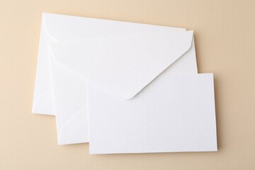 Blank greeting card and envelopes on beige background, top view