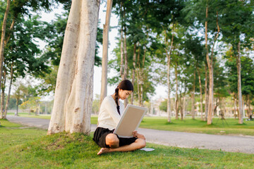 Bathed in warm golden light beneath a tree, a smiling female student immerses herself in her...