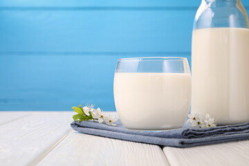 Fresh milk and blossoms on white wooden table against light blue background, closeup. Space for text
