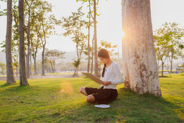 Bathed in warm golden light beneath a tree, a smiling female student immerses herself in her...