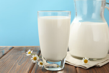 Fresh milk and flowers on wooden table against light blue background, closeup