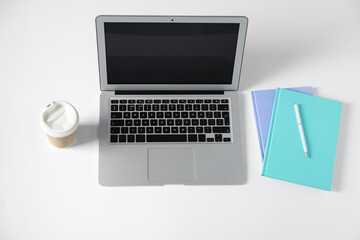Office supplies, laptop and takeaway paper cup on white table, above view