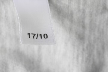 Clothing label with size on light grey garment, closeup. Space for text