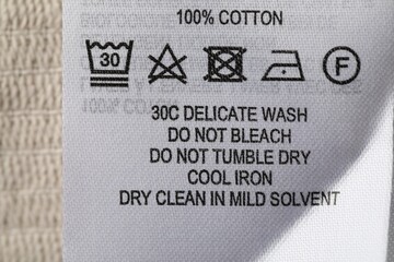 Clothing label with care symbols and material content on beige garment, top view