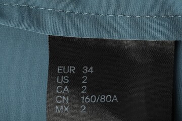 Clothing label with size on light blue garment, top view