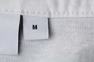 Clothing label with size on white garment, top view. Space for text