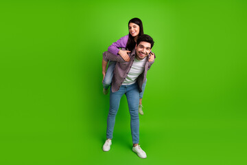 Young couple having fun with a playful piggyback ride on a green background, showcasing a sense of...