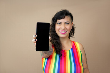 Happy half-shaved hairstyle tattooed woman holding a mobile phone. Perfect for mockup related to LGBTQ+ pride, alternative lifestyle and event annoucement. Copy space available on beige background.
