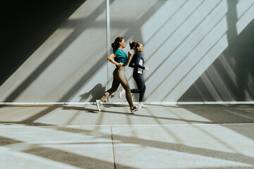 Two women running energetically in the morning light, casting dynamic shadows on the pavement in an...