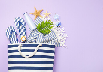 Blue beach bag with summer accessories on color background, top view