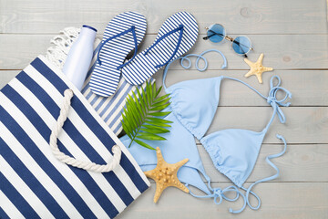 Blue bikini with beach accessories on wooden background, top view