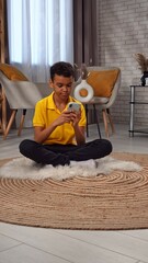 Young african american child boy spending free time at home, kid sits on the floor in the living...