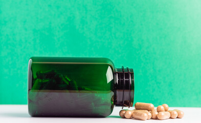 Green Bottle with Capsules on White Surface Against Green Background
