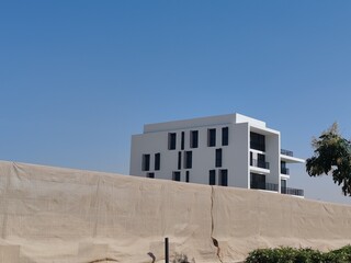 Full View White Color Building With Black Windows And Blue Sky Background.
Highrise Tower or Sky Scraper, Building Outdoor Exterior View With Balcony And Terrace PentHouse Apartment Top Floor Building
