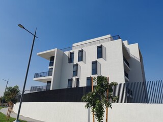 Full View White Color Building With Black Windows And Blue Sky Background.
Highrise Tower or Sky Scraper, Building Outdoor Exterior View With Balcony And Terrace PentHouse Apartment Top Floor Building