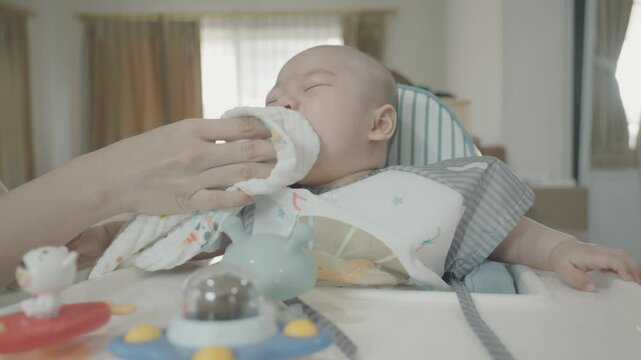 A gentle moment of nurturing as a caregiver wipes a baby's mouth during mealtime. The setting is cozy, promoting warmth and care.