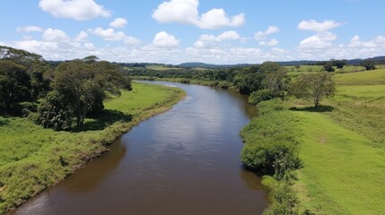 Serene river flowing through lush green pastures under a blue sky with fluffy clouds.