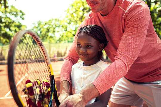Tennis coach teaching young girl how to hold racket during lesson on sunny day