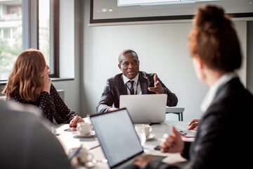 Black businessman leading meeting with diverse colleagues in modern office boardroom