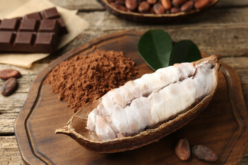 Cocoa pod with beans, powder and chocolate on wooden table, closeup