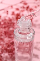Dripping serum from pipette into bottle on blurred pink background, closeup