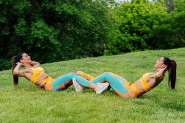 Two fit women doing sit-ups together in a park