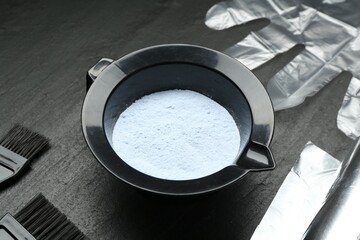 Bleaching powder and hairdresser's tools on black table, closeup