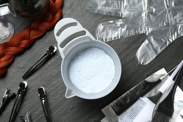 Bleaching powder and hairdresser's tools on black table, flat lay