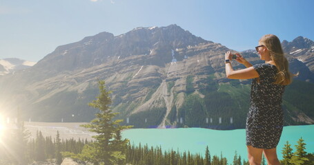 Image of light over caucasian woman taking pictures of mountain landscape