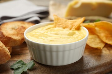 Tasty cheese dipping sauce in bowl, nacho chips and croutons on table, closeup