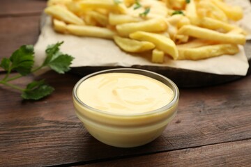 Delicious cheese sauce in bowl, French fries and parsley on wooden table, closeup